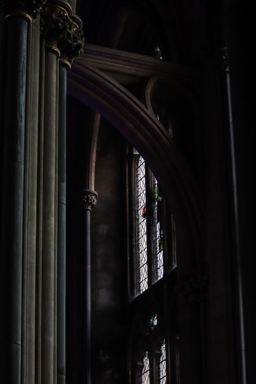Free Moody light illuminates gothic columns and stained glass windows in a cathedral. Stock Photo