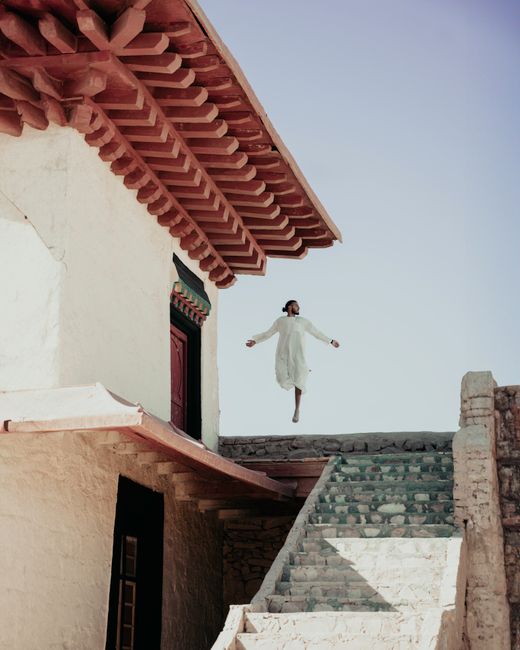 A person leaps in joy near traditional Moroccan architecture in a serene outdoor setting.