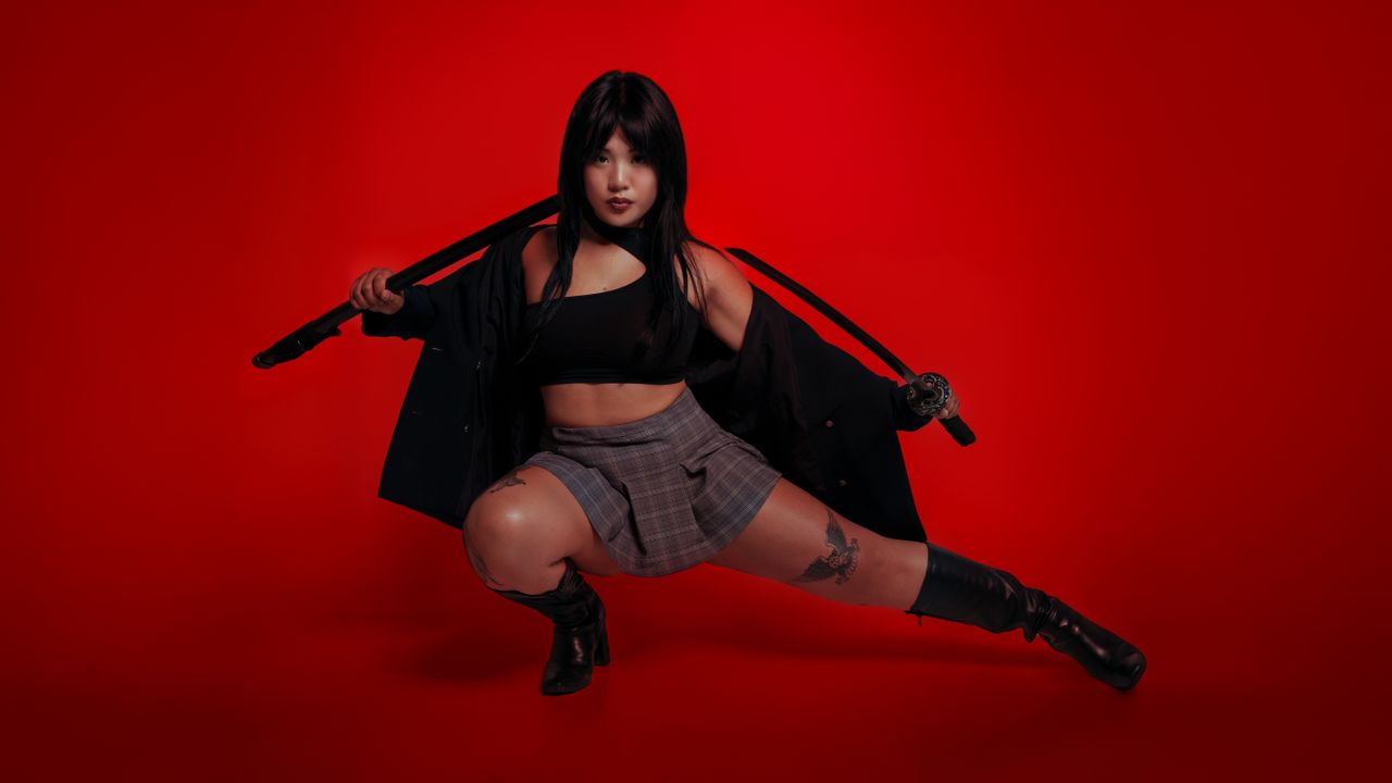 a fierce woman posing with a katana against a red backdrop exuding str