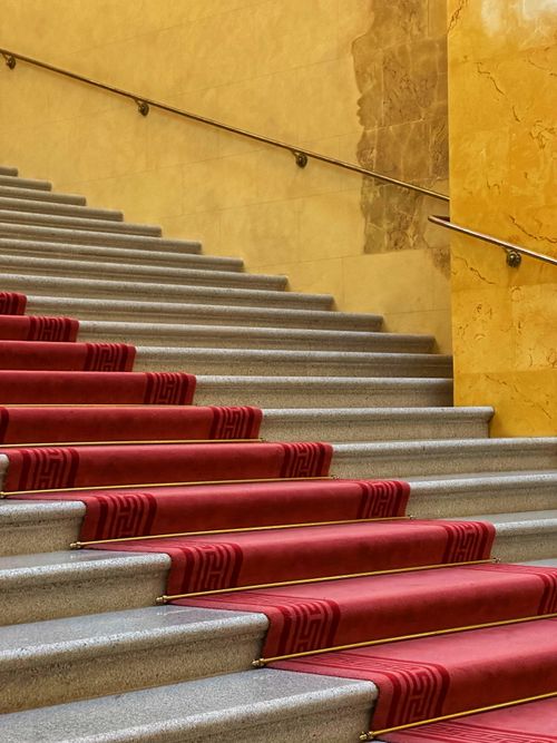 Free Luxurious interior featuring a grand staircase with red carpet and warm lighting. Stock Photo