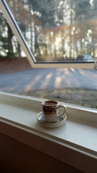 Decorative coffee cup on a window sill with a forest view.