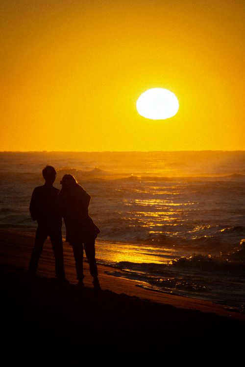 Free Silhouetted couple embracing on a serene beach during a vibrant sunset. Stock Photo