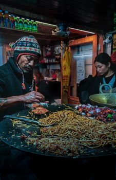 Street food vendor preparing noodles and roast in a bustling market in Sikkim, India.