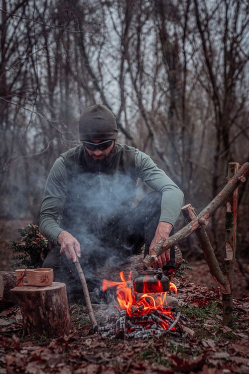 Free A man skillfully builds a campfire in a dense forest, showcasing survival techniques. Stock Photo