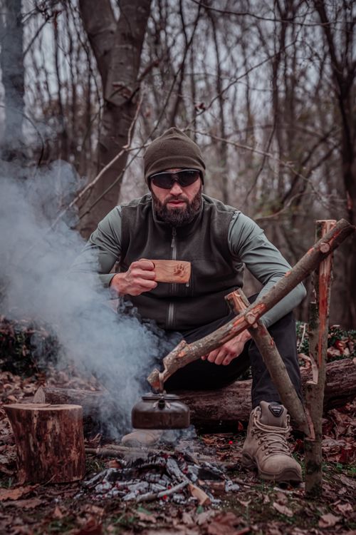 Free A man enjoying coffee by a campfire in a serene forest setting, showcasing outdoor adventure. Stock Photo