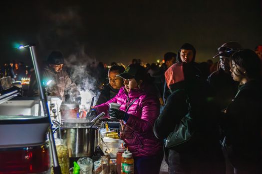 Vibrant night market with people gathered around a steaming food stall.