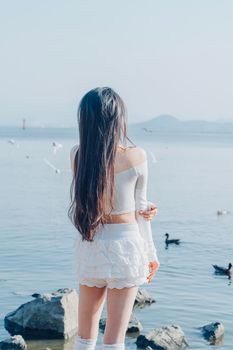A woman gazes at a tranquil lake, surrounded by birds and a clear blue sky.