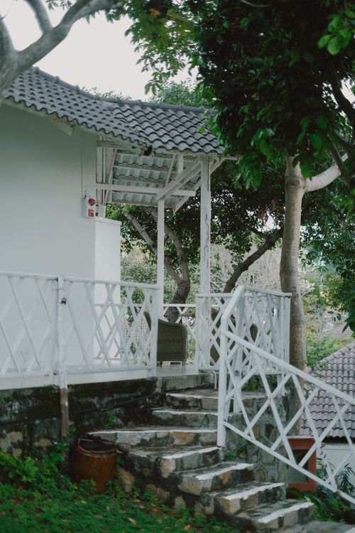 Free A quaint white house with a stone path surrounded by lush greenery, evoking a serene atmosphere. Stock Photo