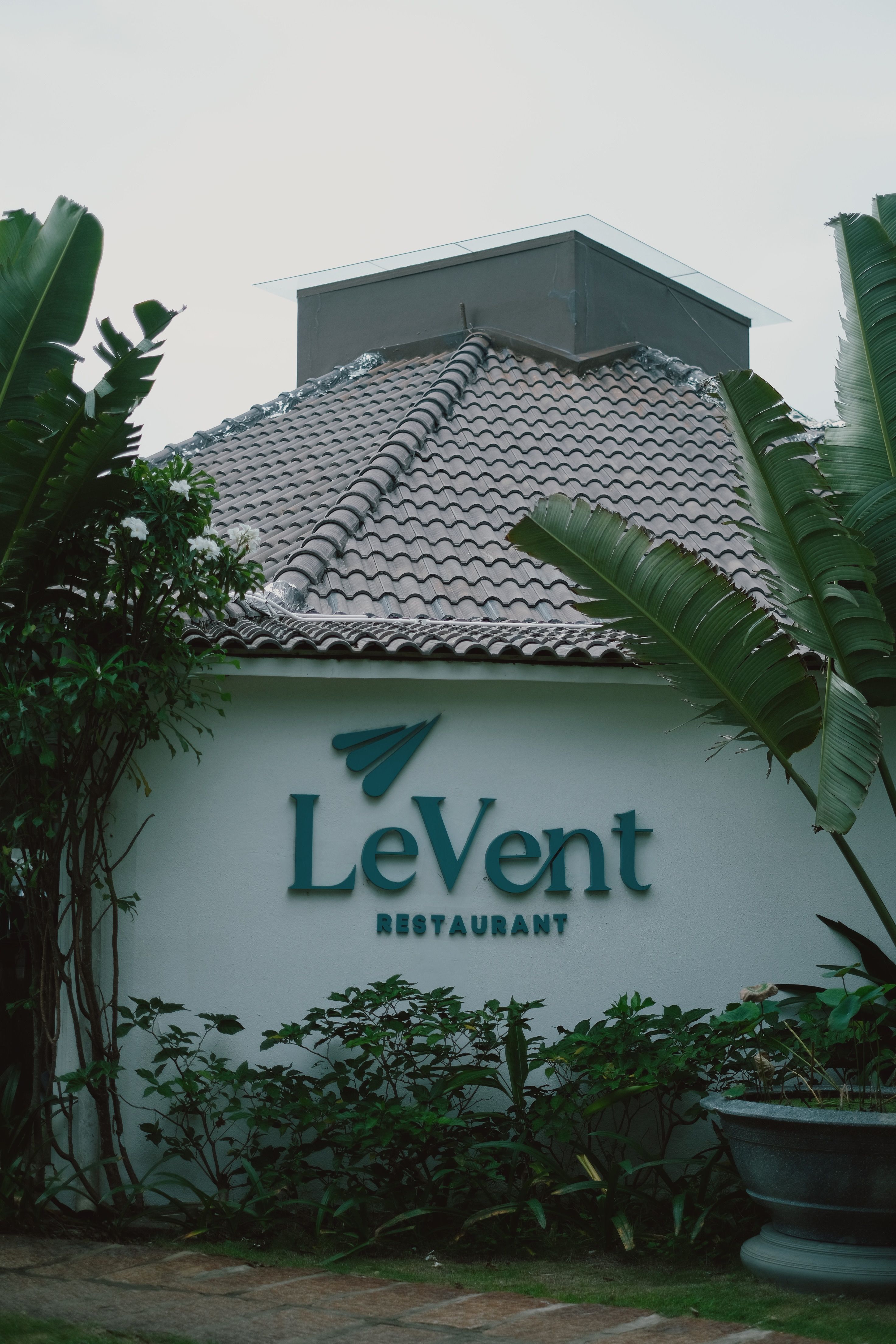 The exterior of LeVent Restaurant surrounded by tropical plants, showcasing its unique roof design.