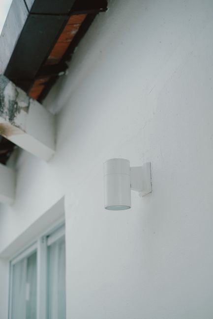 A simple white wall with a modern cylindrical light fixture outdoors.