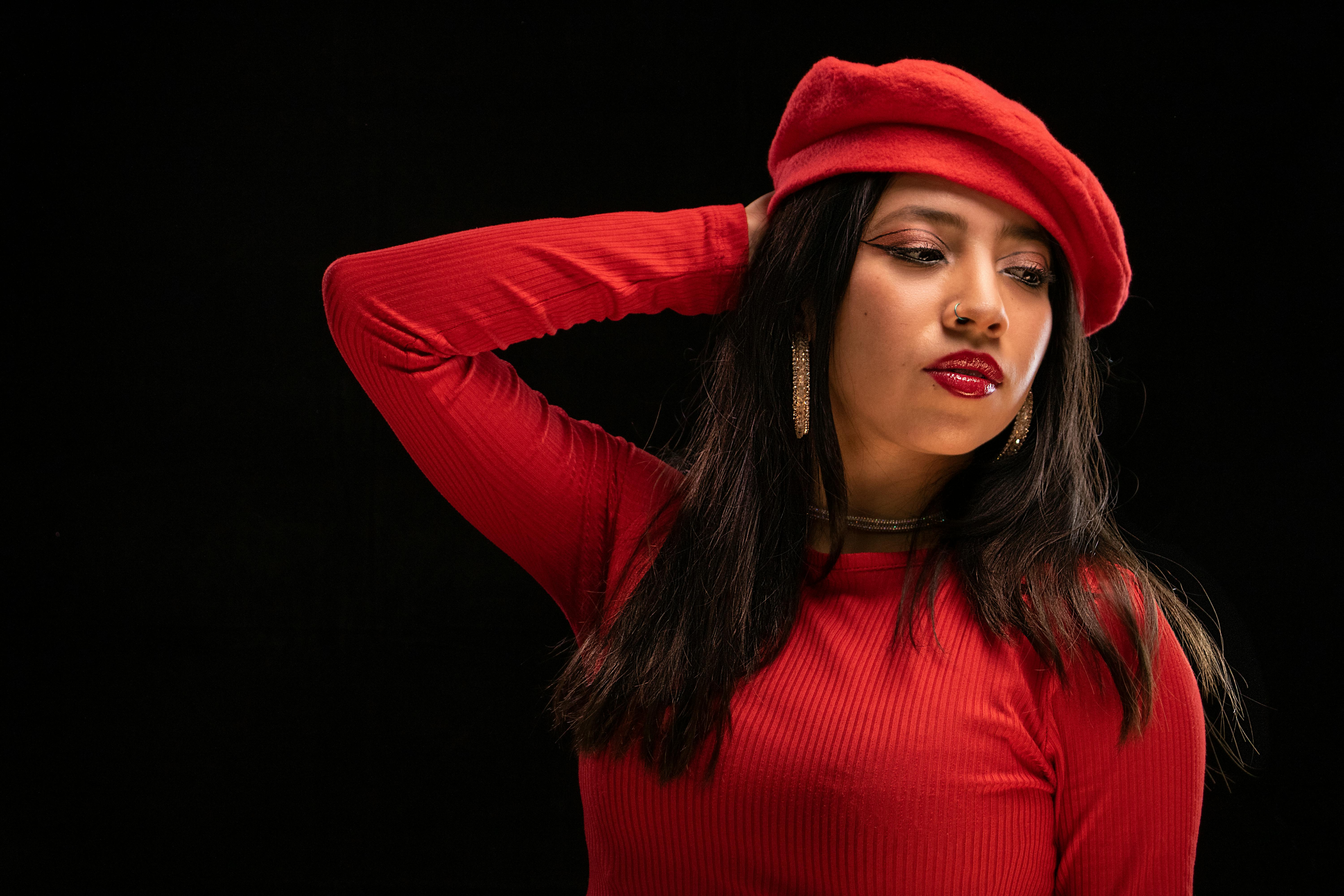 Stylish woman wearing red dress and beret posing against dark background.