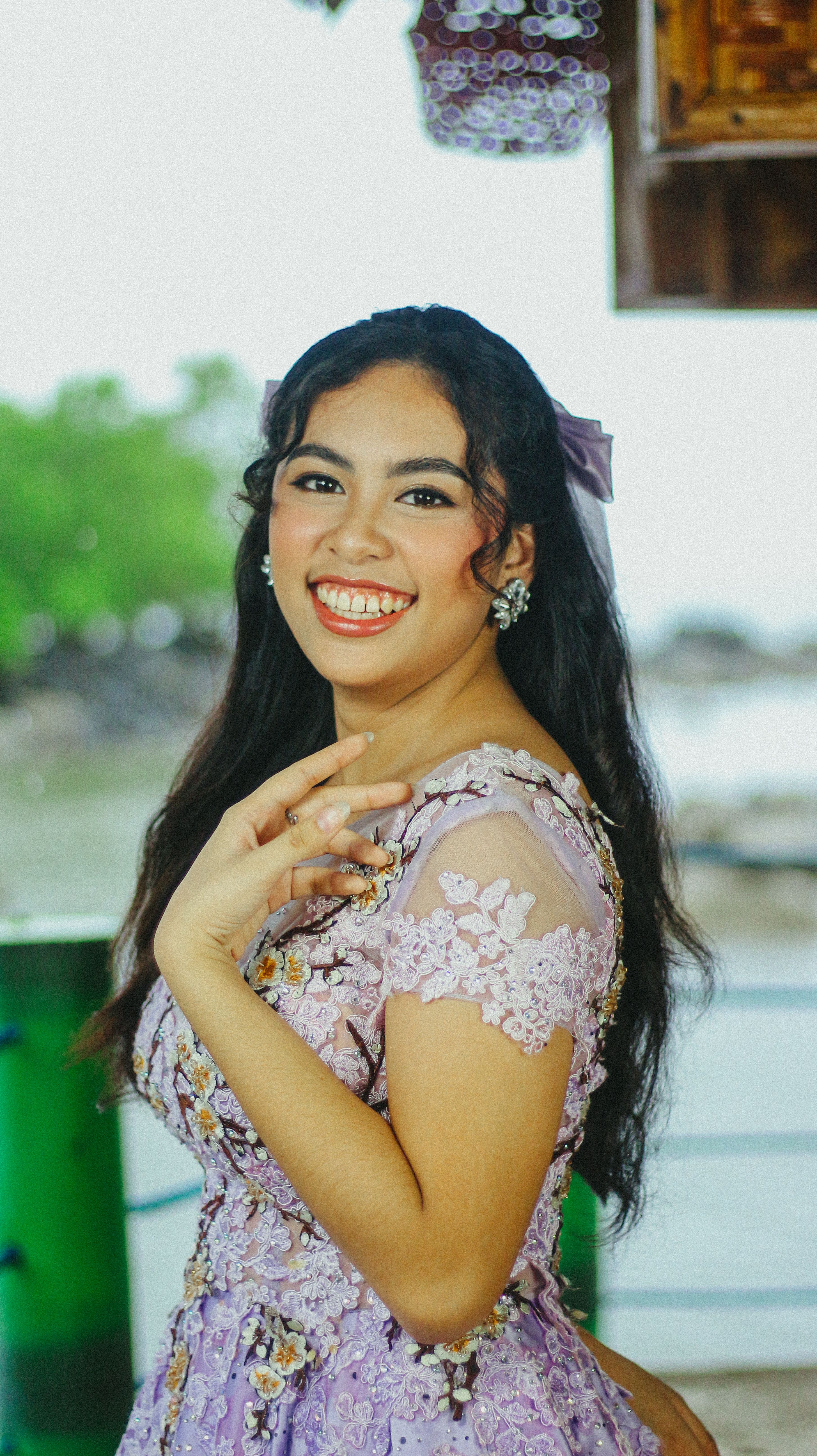 A joyful woman in a floral lavender dress smiles brightly outdoors with a natural backdrop.