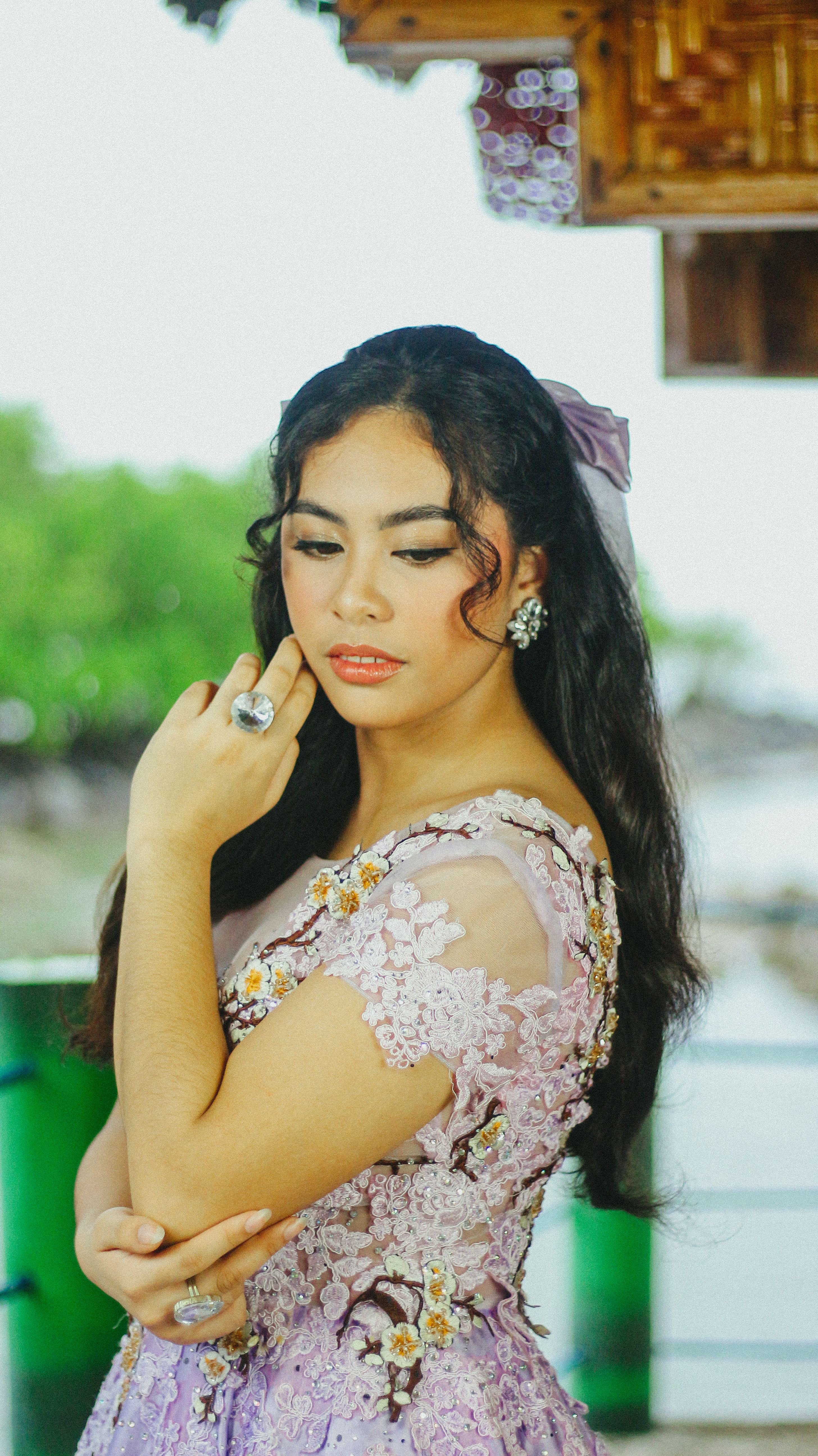 Elegant portrait of a young woman in a lavender dress with intricate floral designs, posing gracefully.