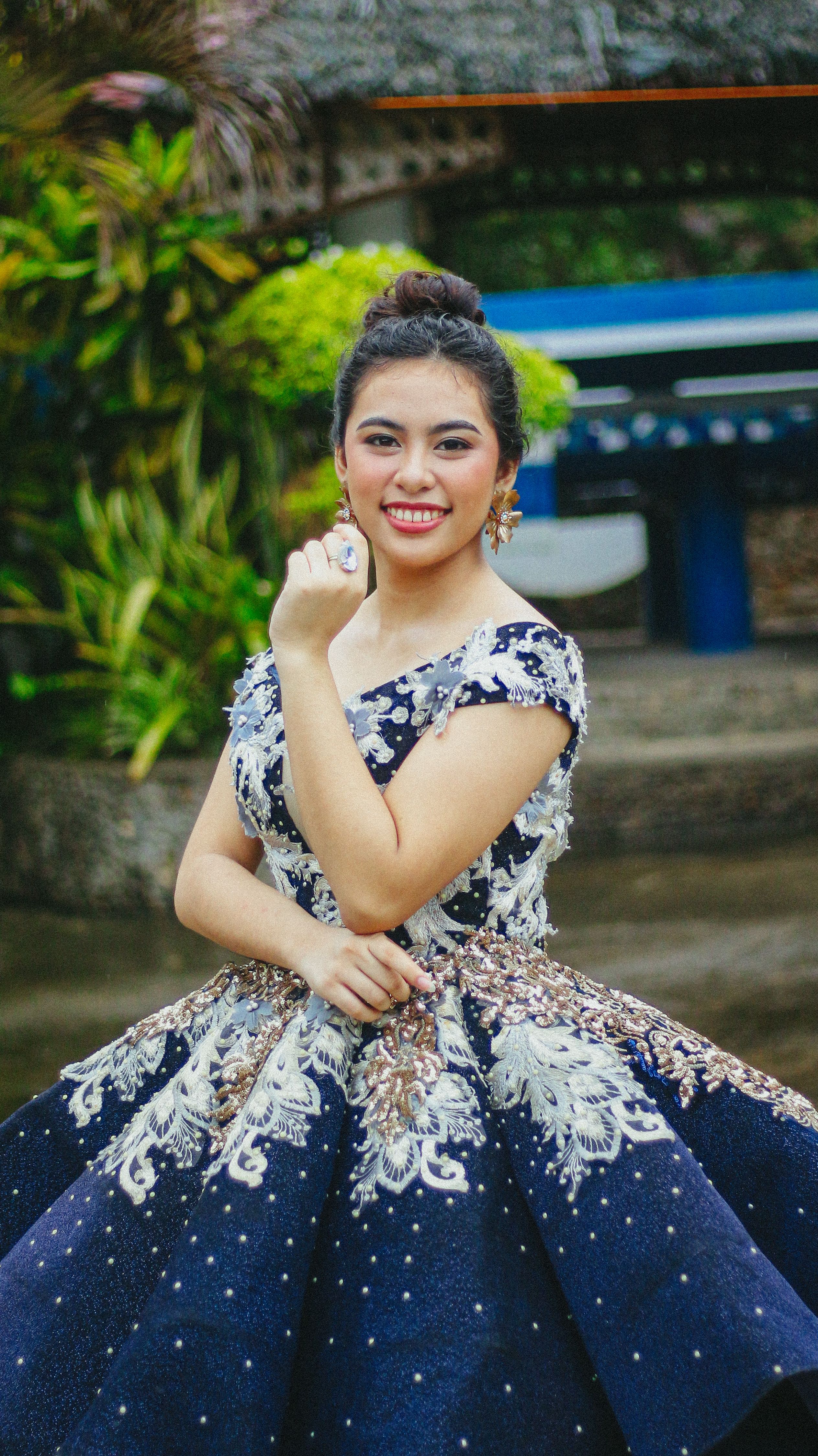 Young woman in a glamorous, patterned gown posing outdoors with a smile.