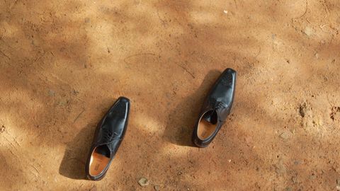 A pair of black leather shoes laid on an earthy surface under sunlight.