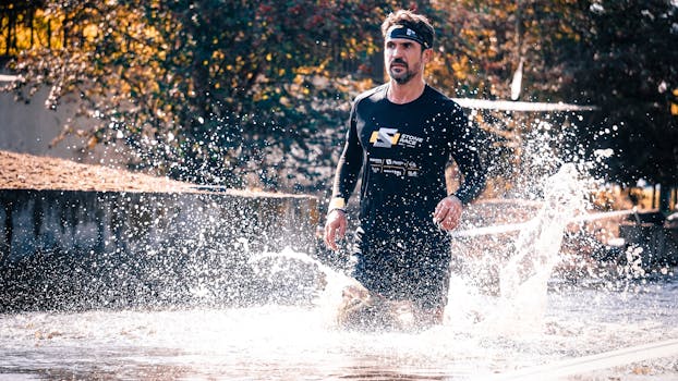 Athlete running through water splash during outdoor obstacle race.