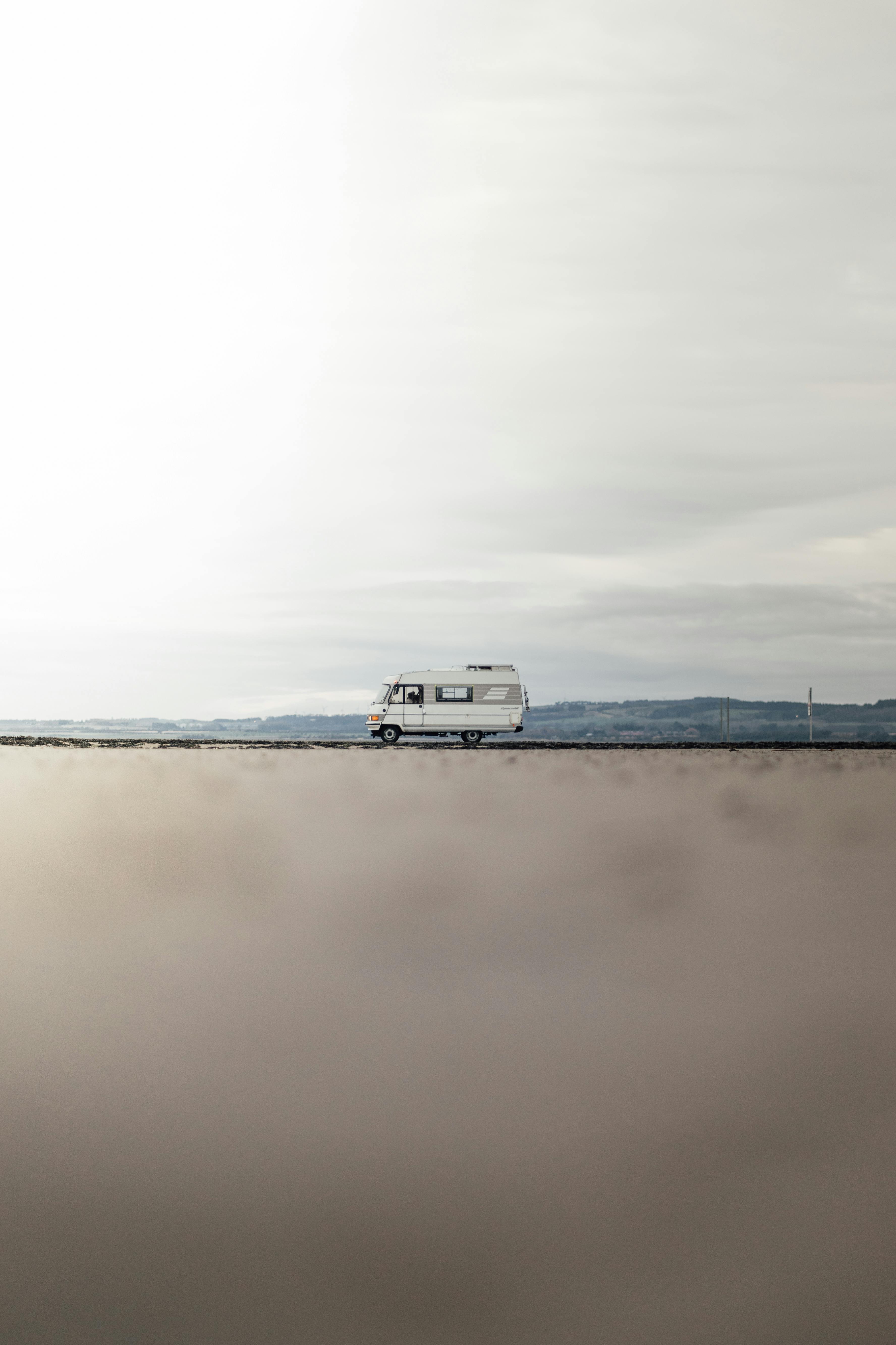 Ücretsiz Uzaktaki tepelerin ardında sisli bir İskoç yolunda ilerleyen bir karavanın minimalist görüntüsü. Stok Fotoğraflar