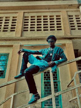 A fashionable adult sitting on a building's railing with a cool and relaxed demeanor.
