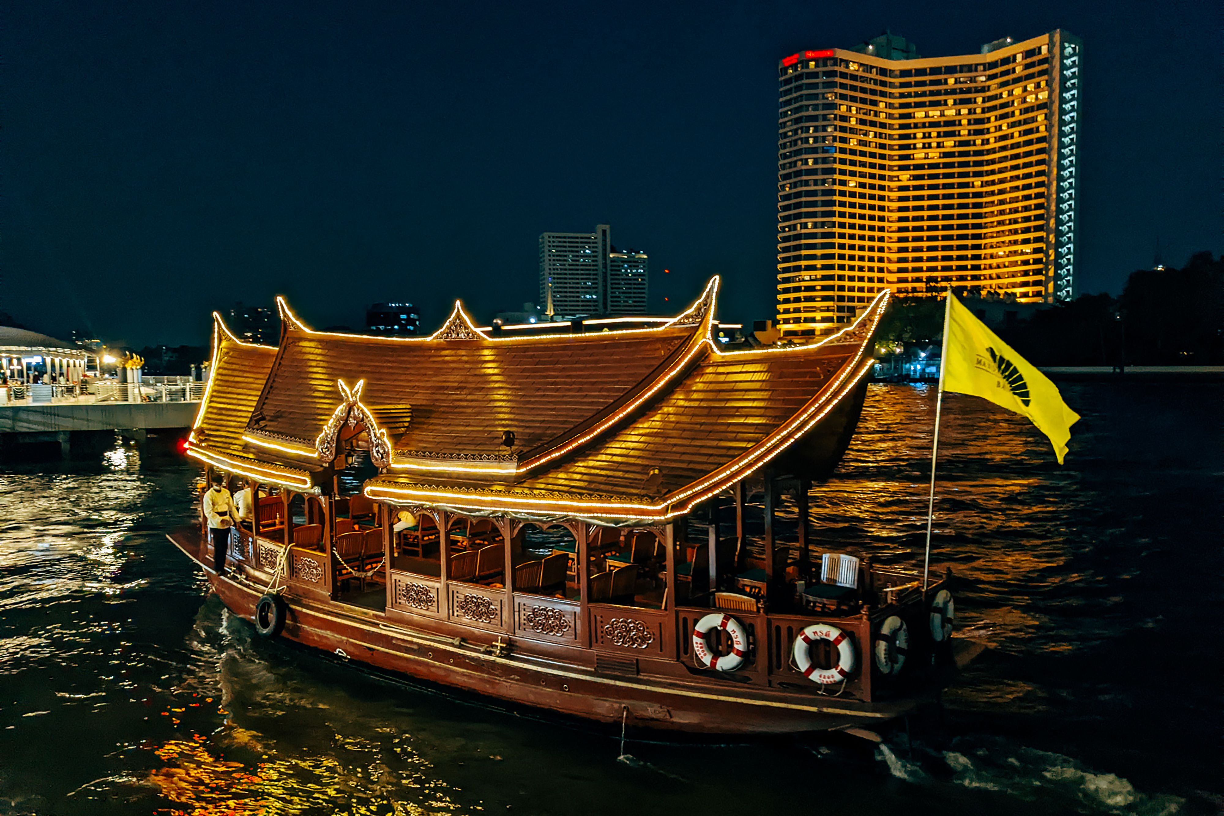 A traditional wooden Thai boat lit up on a river at night.