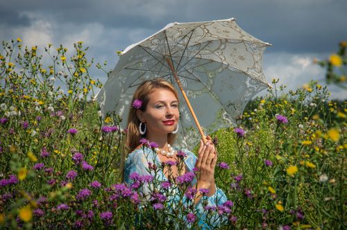 Free A woman with a parasol stands in a vibrant wildflower field under a dramatic sky. Stock Photo