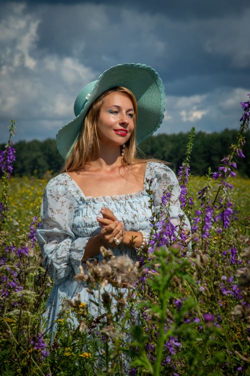 Free Woman in a floral meadow wearing a blue sun hat and floral dress, embracing nature. Stock Photo
