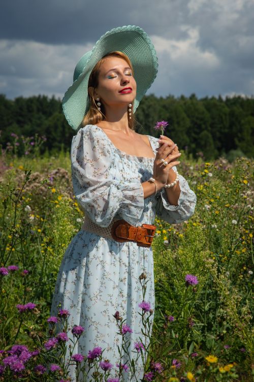 Free A woman in a floral dress and sun hat enjoying a vibrant meadow on a sunny day. Stock Photo
