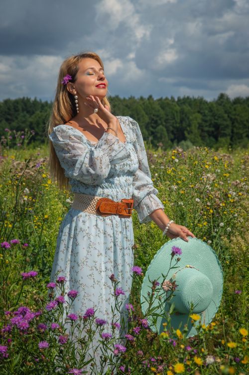 Free Woman in a floral dress and hat enjoying a sunny day in a blooming flower field. Stock Photo