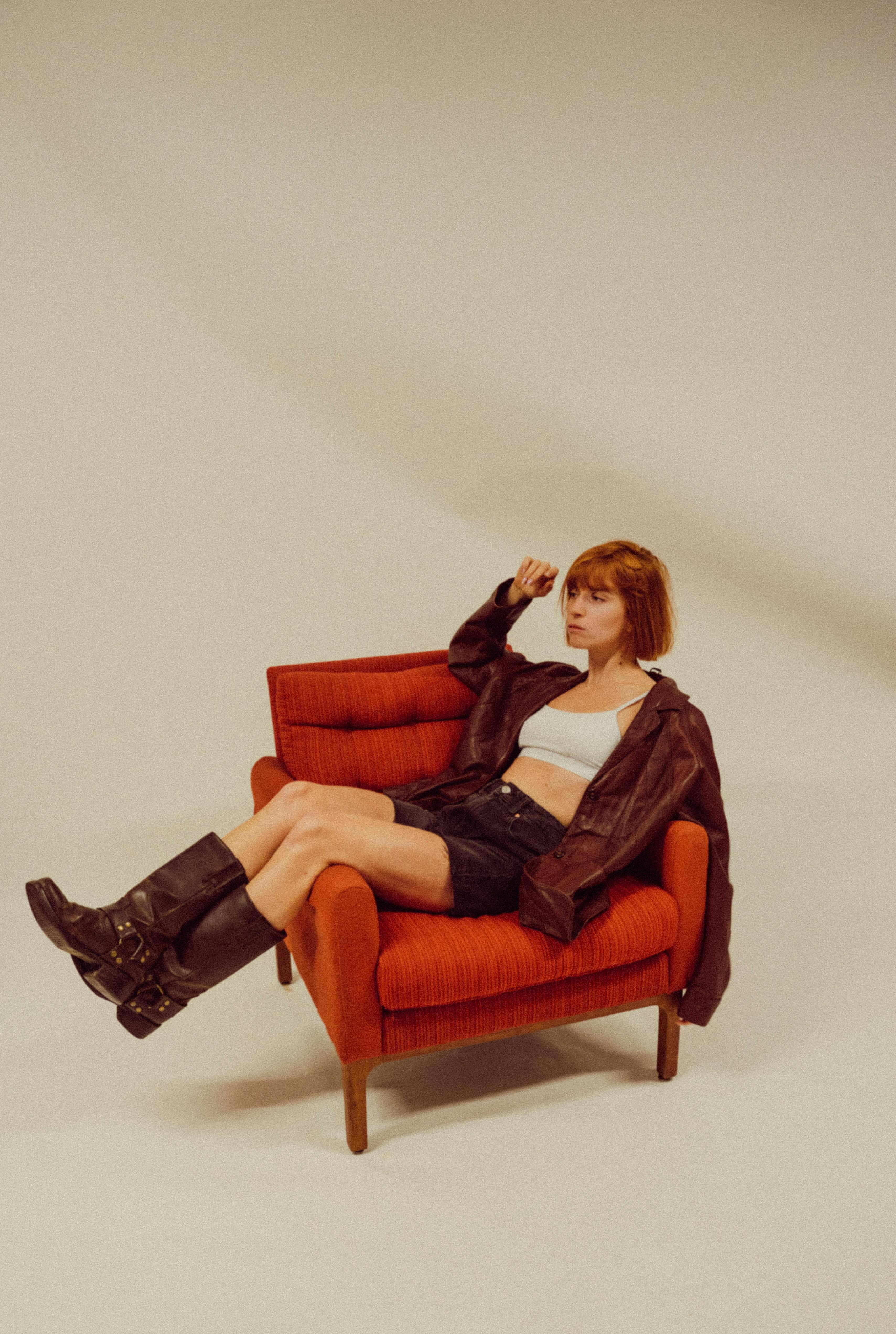 Trendy woman in stylish outfit sitting on a retro armchair, exuding vintage charm.