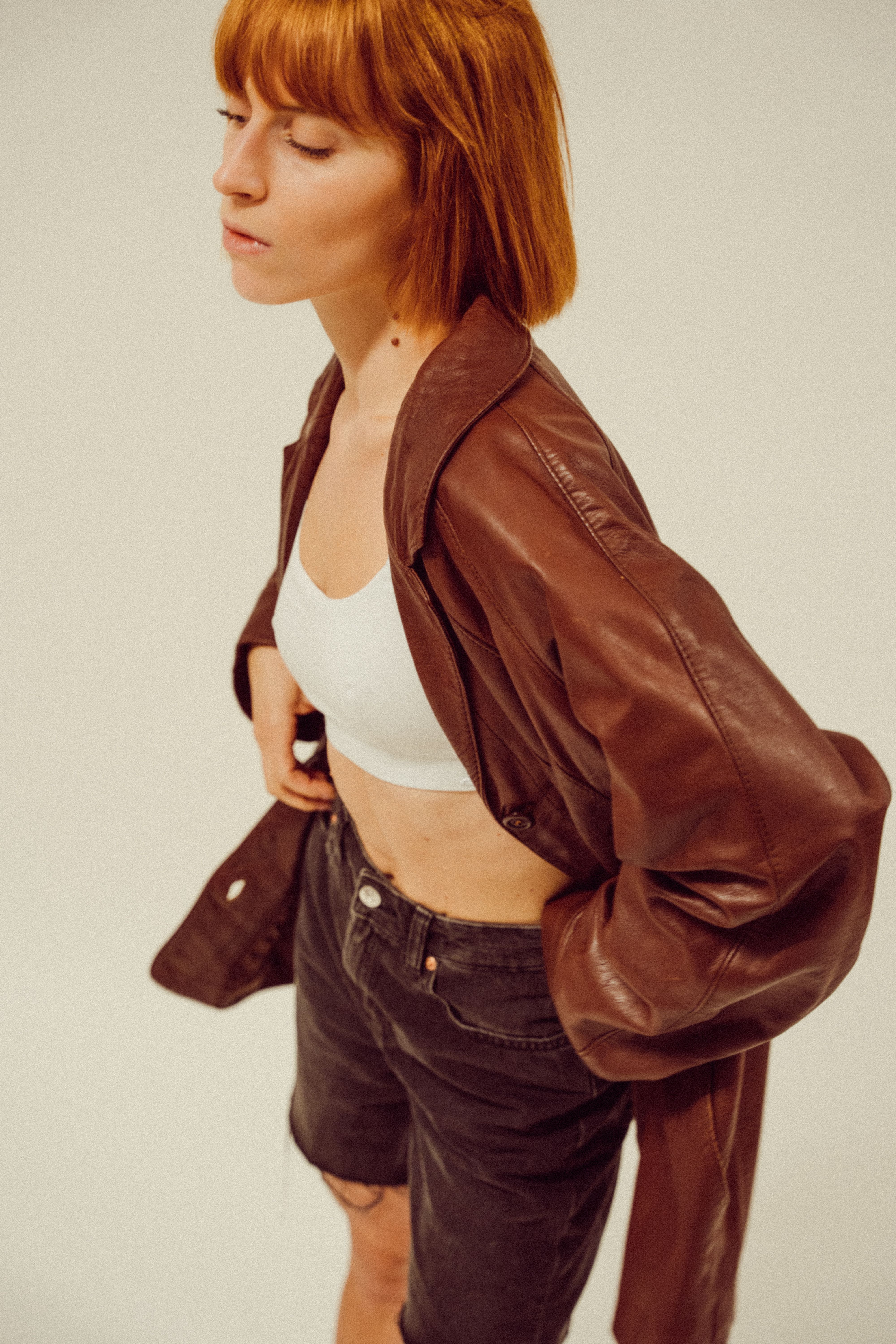 Young woman in a vintage leather jacket posing with confidence in studio lighting.