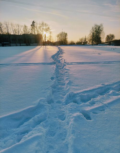 Free A serene snowy pathway with a vibrant sunset in the background, capturing the winter's peacefulness. Stock Photo