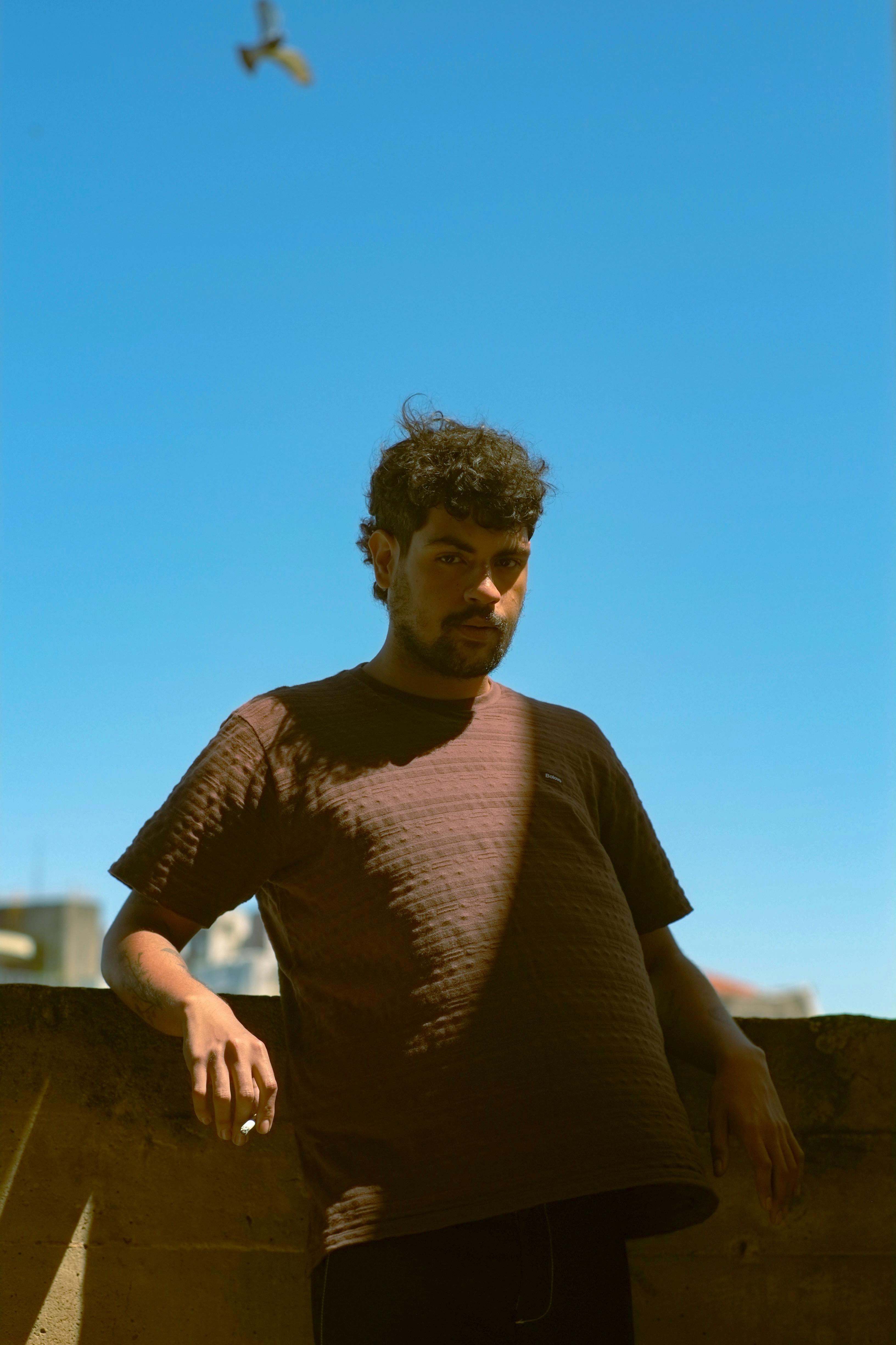 Casual portrait of a man outdoors with clear blue sky and city in background.