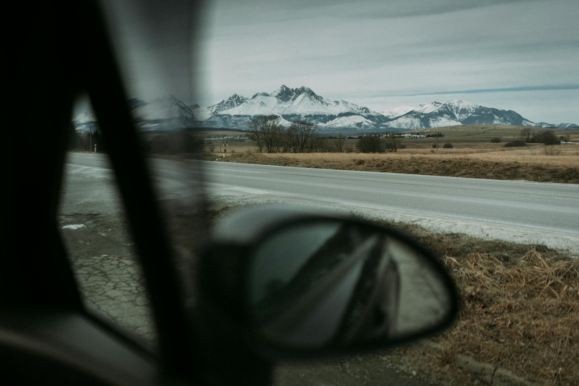 Captivating view of snow-capped mountains through car side mirror on a road trip adventure.