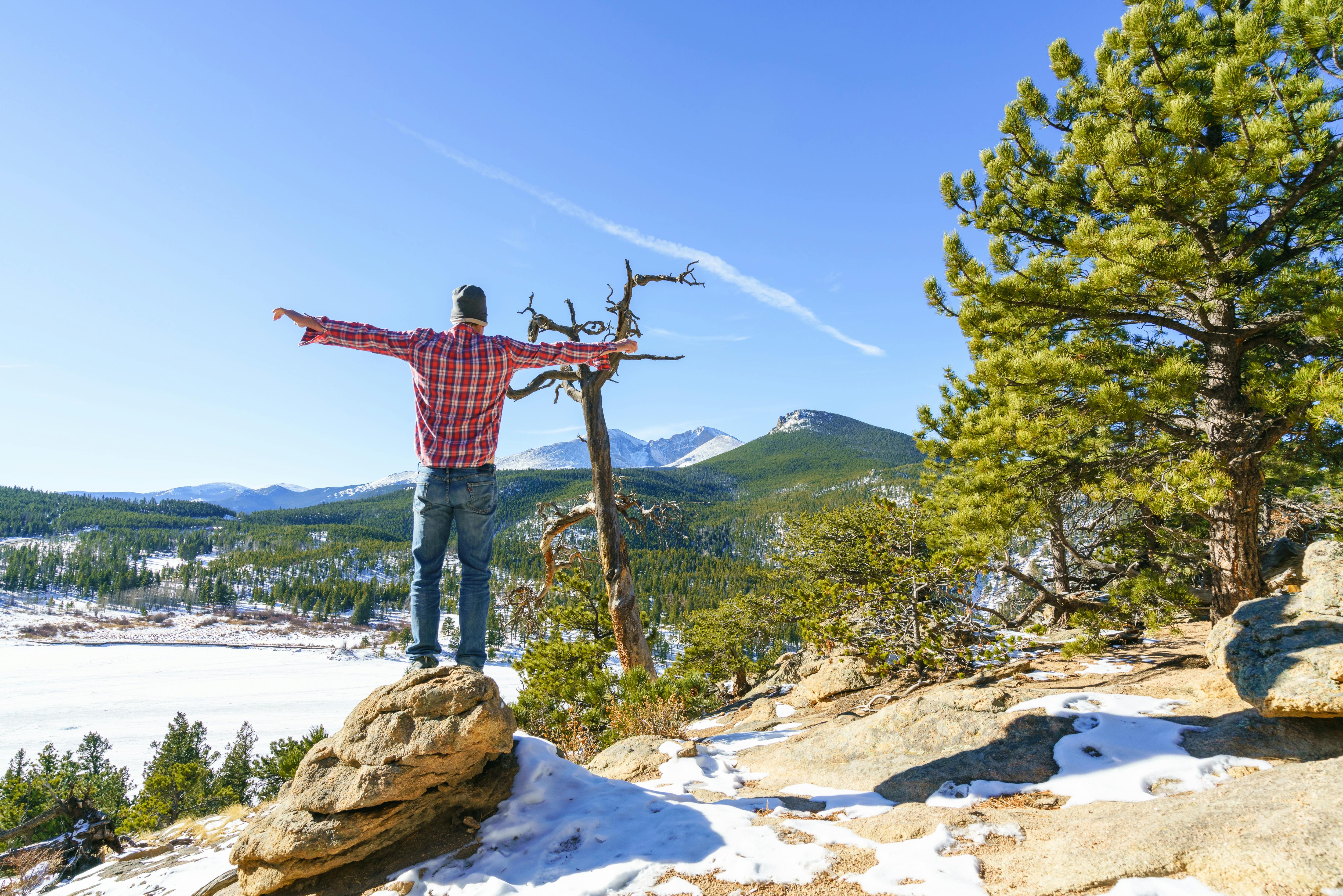 A hiker stands on a rock overlooking a snowy landscape in Colorado.