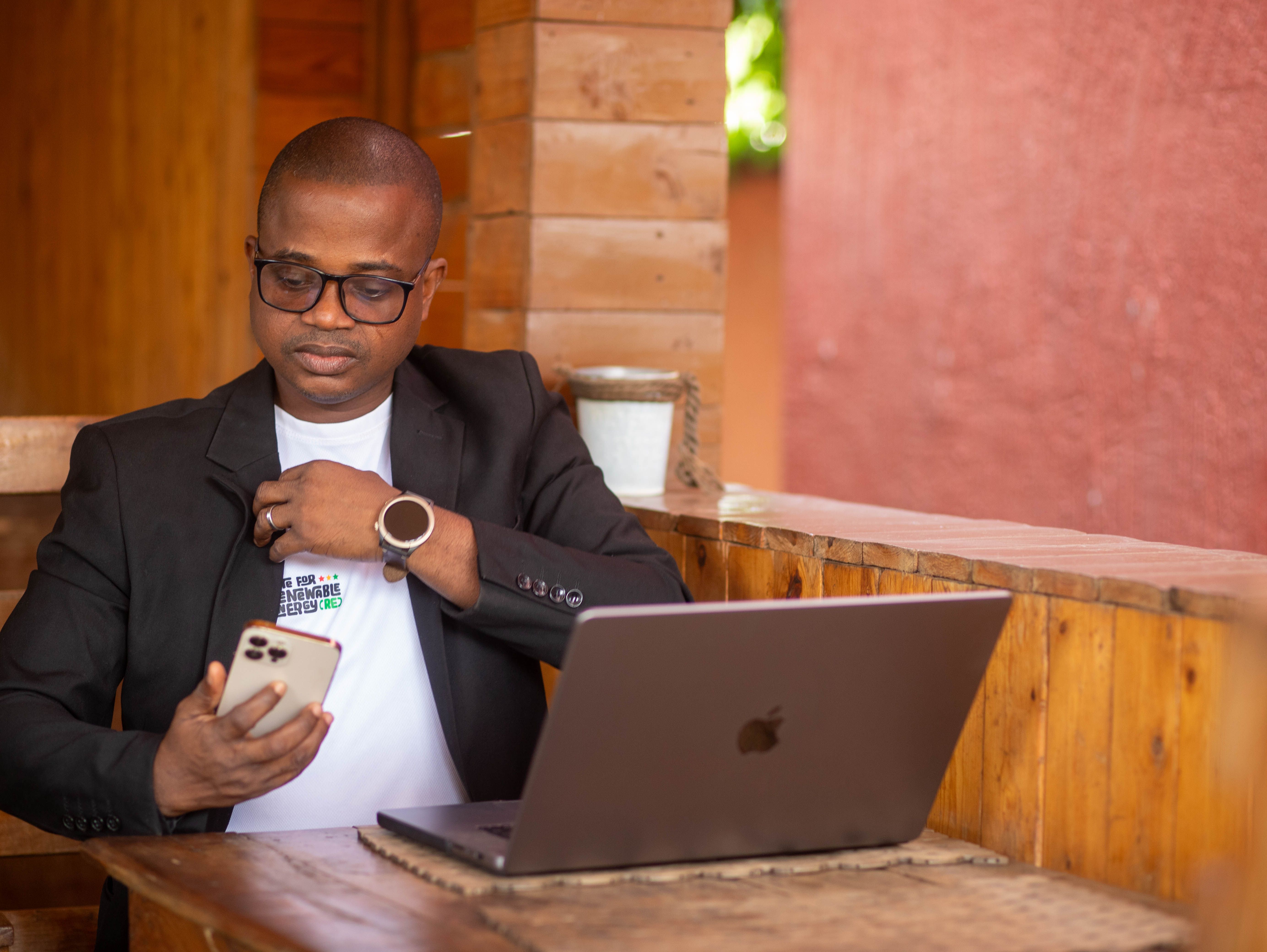 A focused businessman multitasking with a smartphone and laptop in a casual workspace.