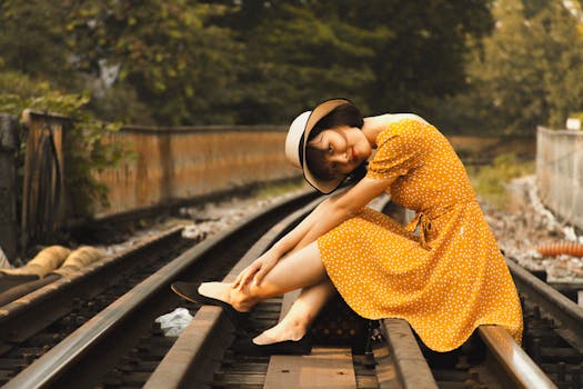 Young woman in polka dot dress and hat sitting on train tracks, smiling.