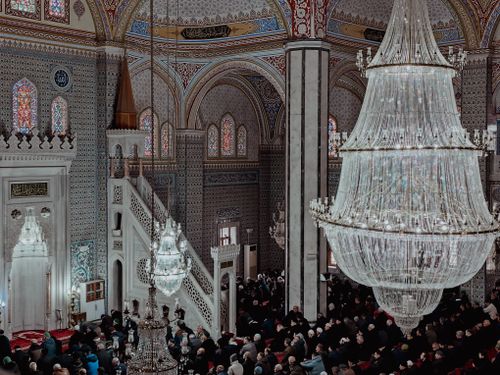 Free A stunning view of a mosque interior with worshippers gathered under ornate chandeliers. Stock Photo