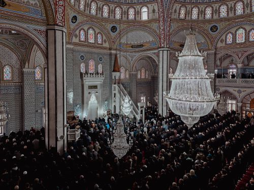 Free A large congregation gathers inside a beautifully decorated mosque under grand chandeliers. Stock Photo