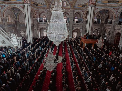 Free Aerial view of a large congregation praying inside an ornate mosque with chandeliers. Stock Photo