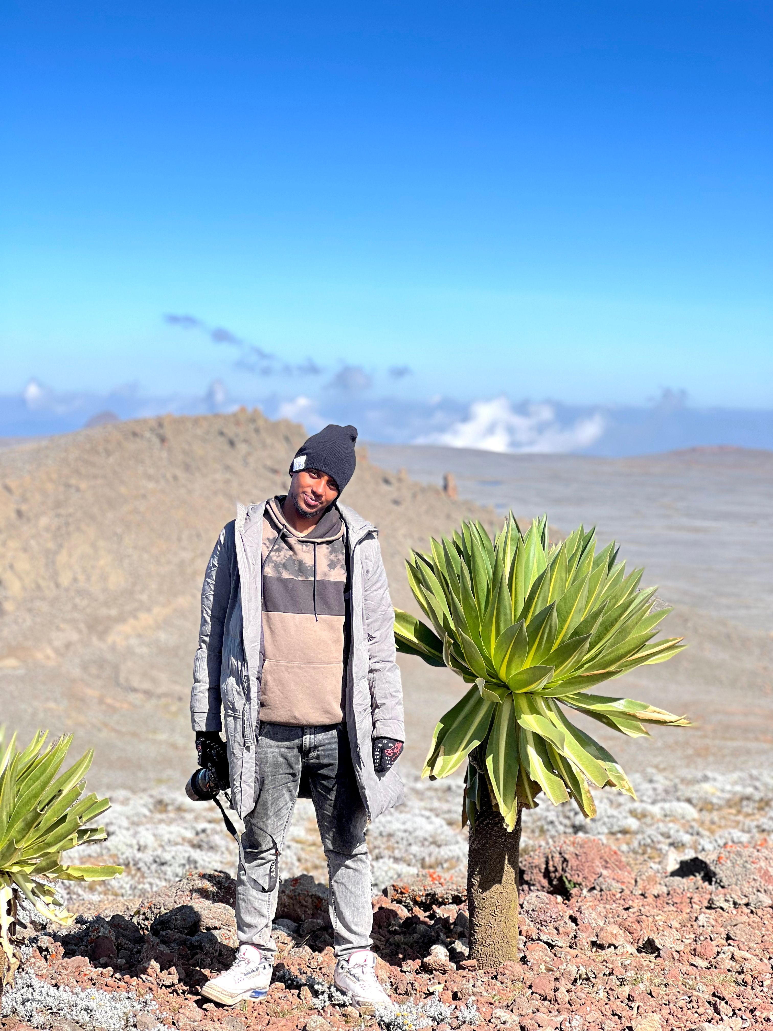 Man in winter attire exploring a mountainous landscape with unique flora.