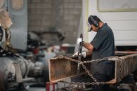 Mechanic engaged in repair work, focused and wearing protective gear in an industrial garage.