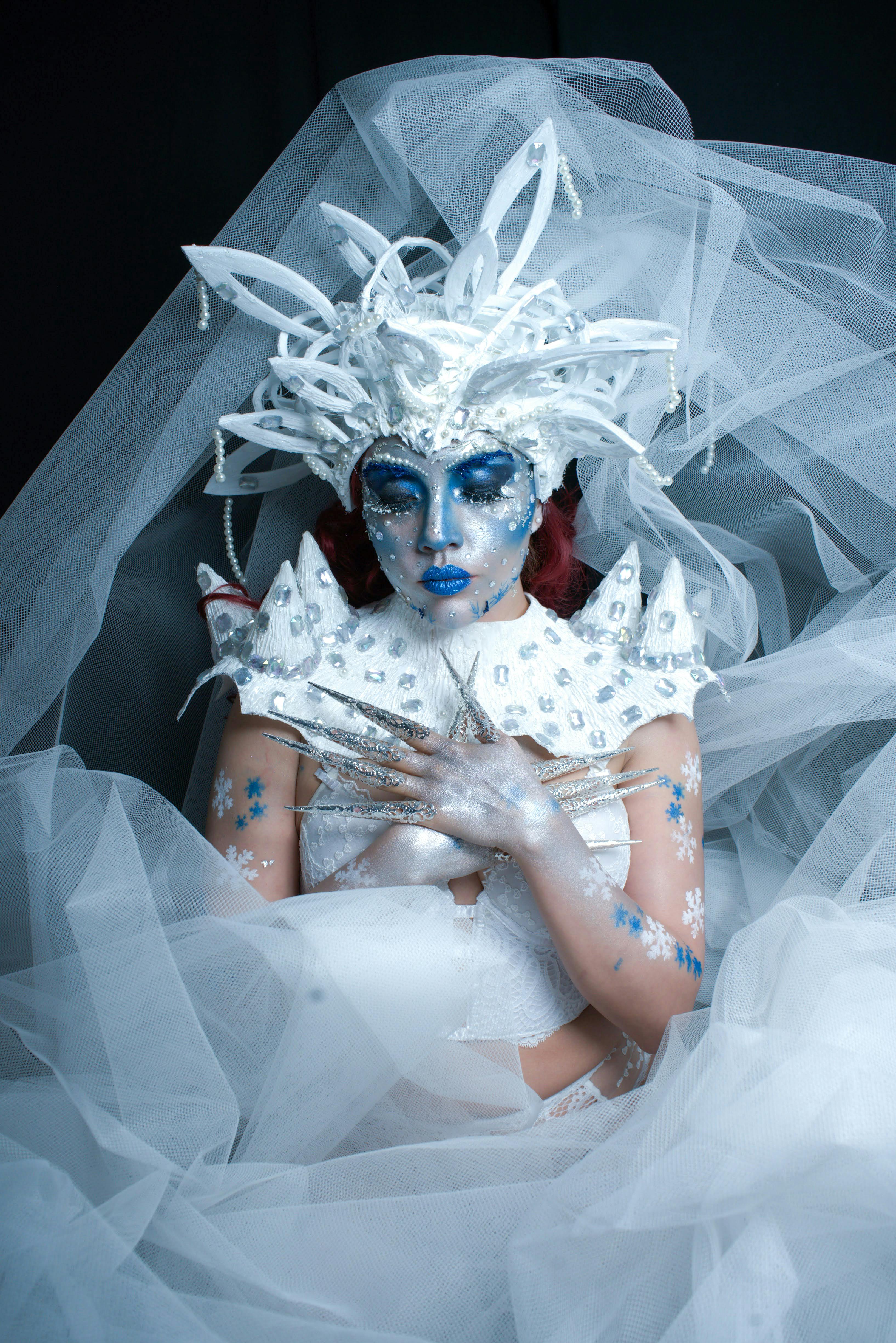 A creative portrait of an ice queen with dramatic white costume and blue makeup.