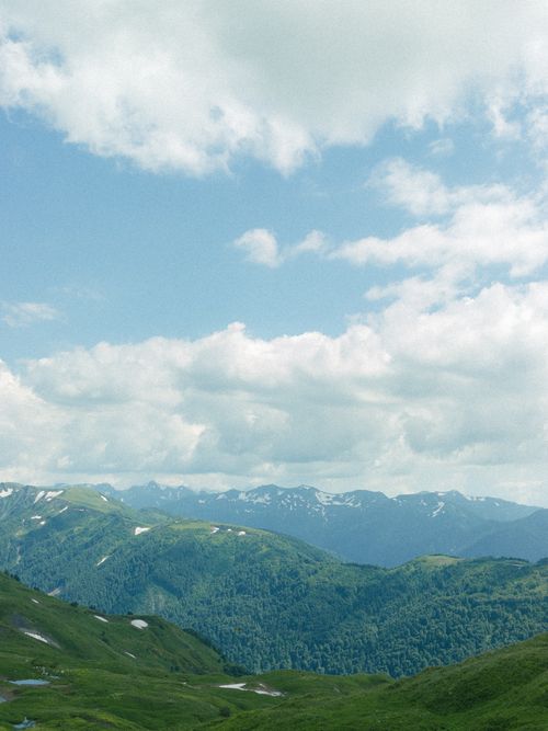 Free Expansive mountainous landscape with lush greenery and a bright blue sky dotted with clouds. Stock Photo