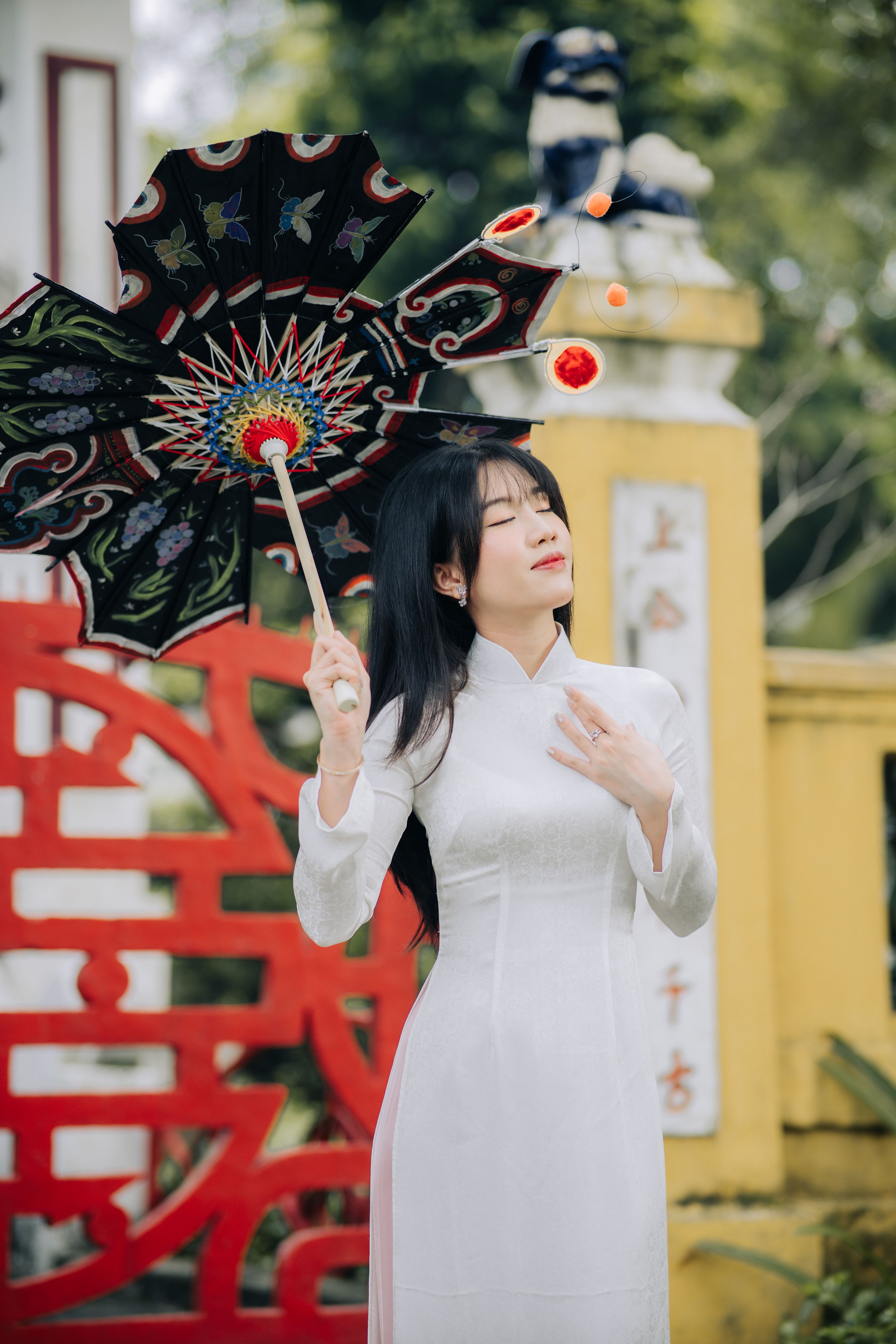 Woman in traditional Vietnamese dress with ornate umbrella in an outdoor setting.