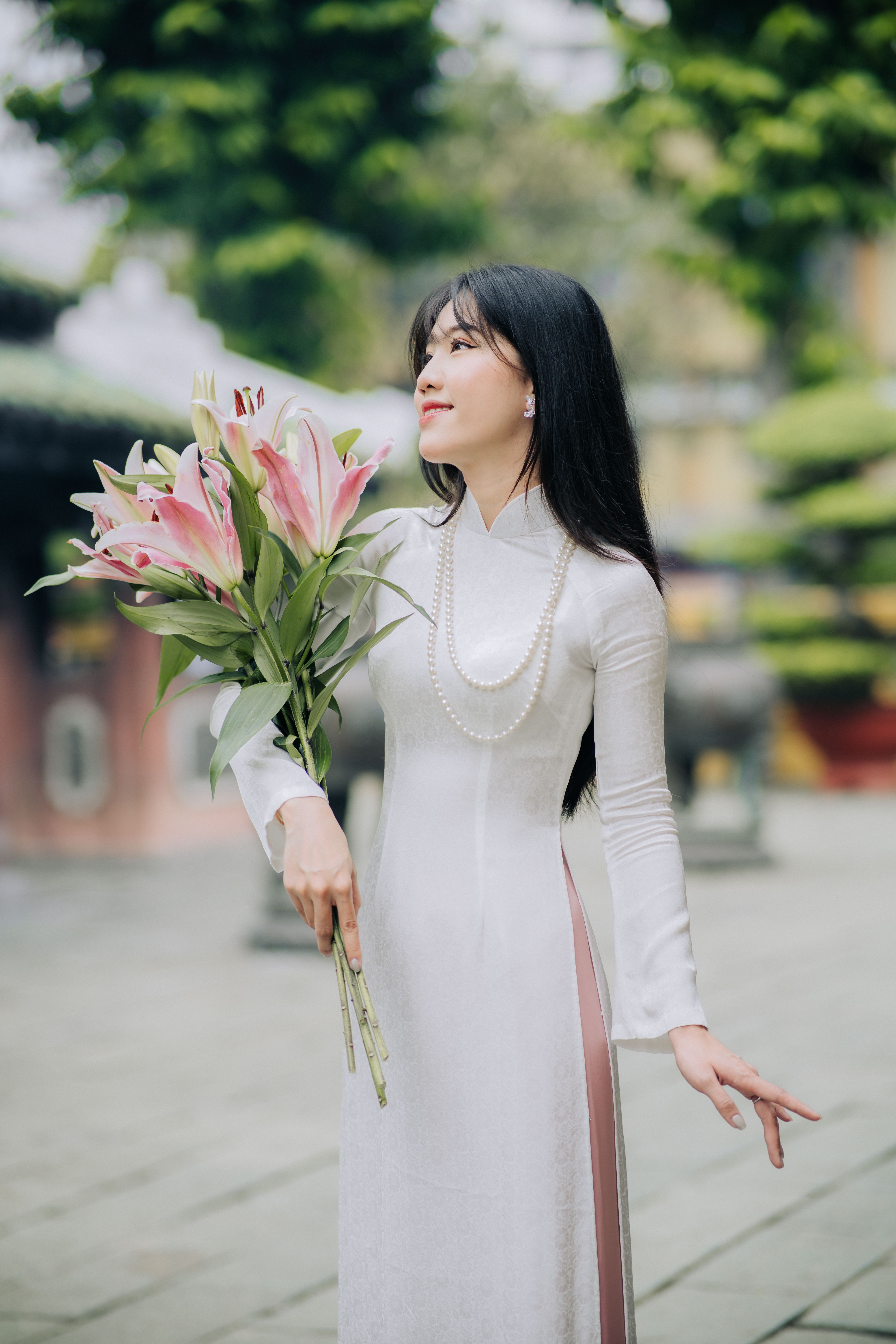 Woman in Traditional Dress Holding Pink Lilies Outdoors · Free Stock Photo