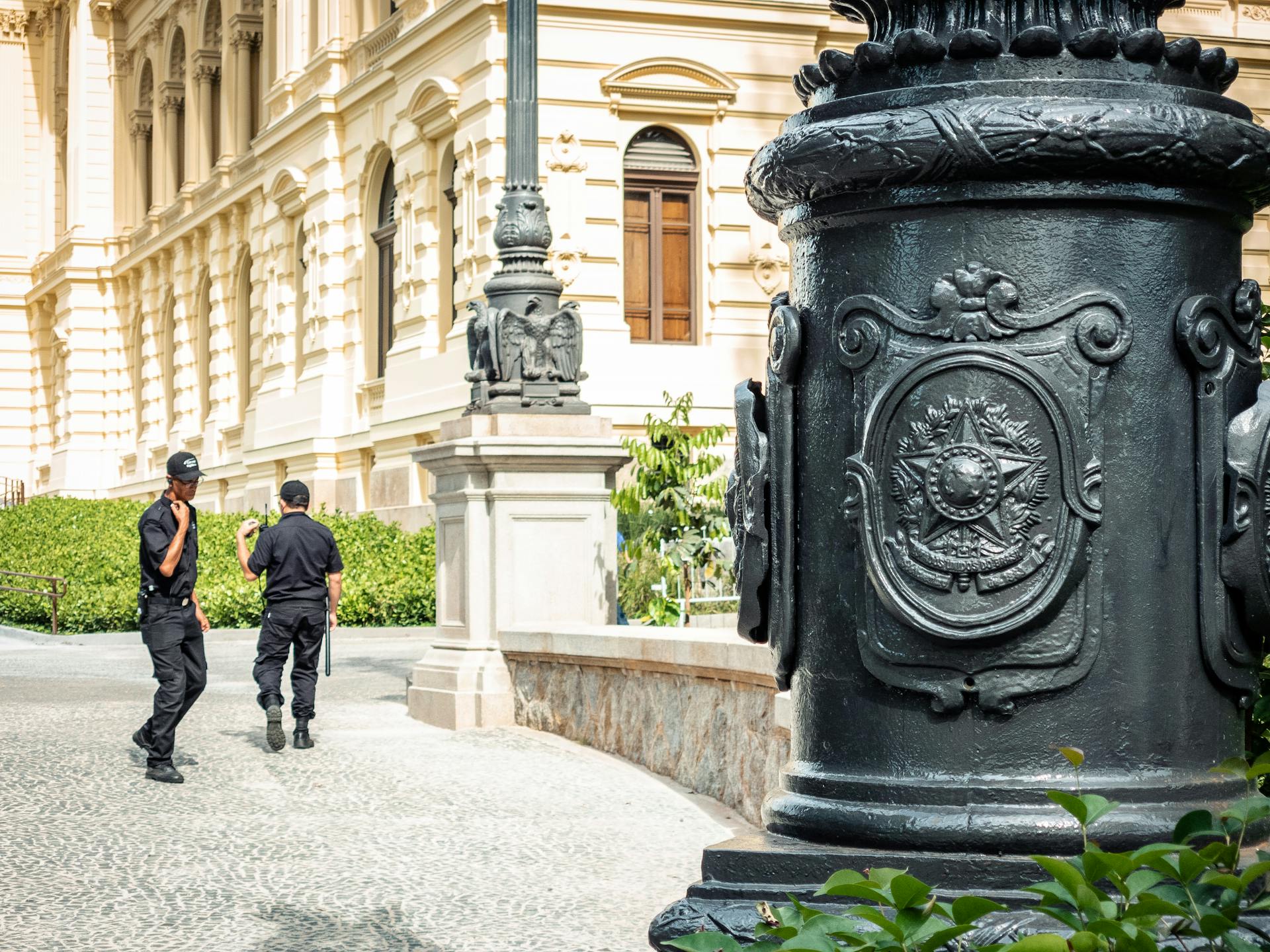 Two security guards patrol in front of ornate historic architecture in São Paulo, Brazil.