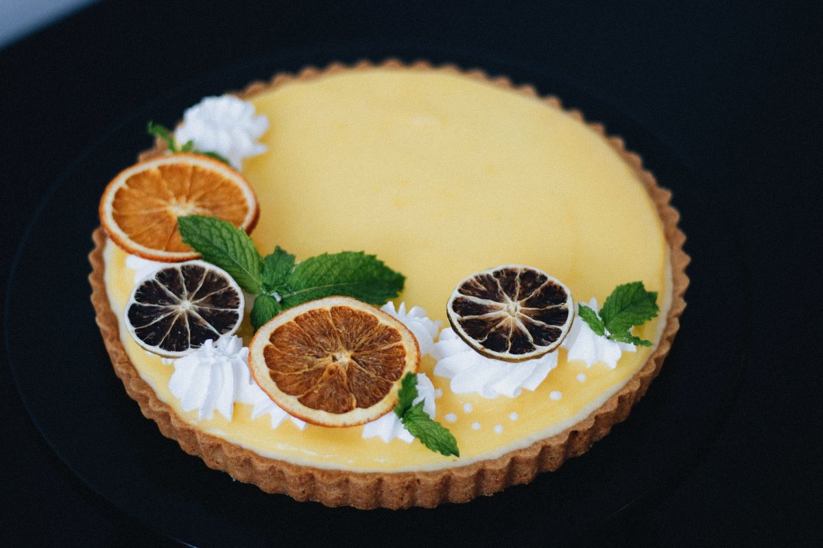 Lemon custard tart decorated with dried orange slices, whipped cream rosettes and mint leaves
