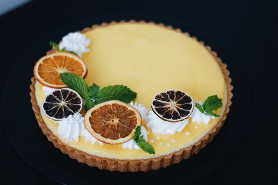 Lemon custard tart decorated with dried orange slices, whipped cream rosettes and mint leaves