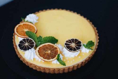 Free Elegant lemon tart garnished with dried citrus slices and mint on a black surface. Stock Photo