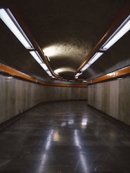 A dimly lit underground tunnel with orange accents and fluorescent lights creating a moody atmosphere.