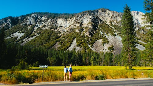 Person Wearing Blue Shirt Standing on Street Beside of Mountain